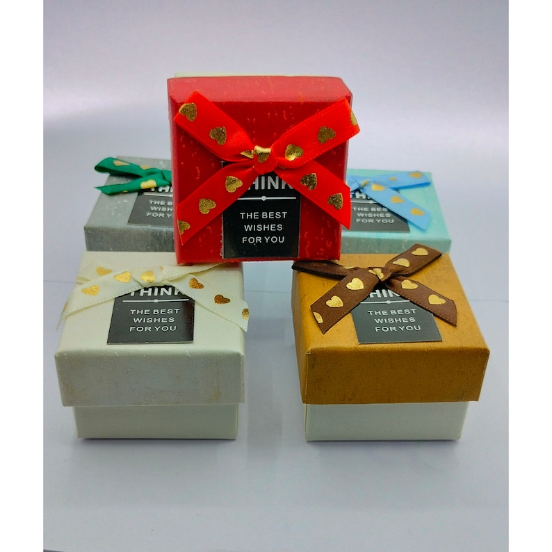 May include: Several small gift boxes in assorted colours, such as red, gold, and blue. Each box is square and decorated with a ribbon featuring heart-shaped details. The boxes have a label that reads "THINK THE BEST WISHES FOR YOU."