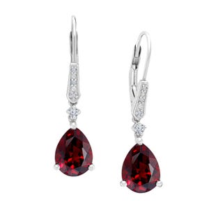 May include: A pair of silver dangle earrings with a pear-shaped red gemstone and small clear gemstones. The earrings have a leverback closure.