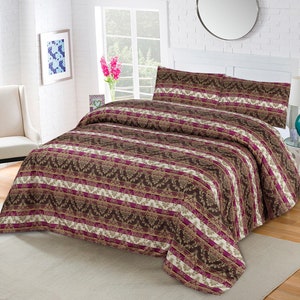 Op de afbeelding: Een bruin en wit beddengoed en kussenset met patronen. Het beddengoed heeft een herhalend ontwerp van bloemen- en streepmotieven in bruin, wit en magenta. Het bed is opgemaakt en klaar voor gebruik.