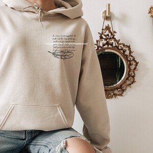 May include: A beige hoodie with a black feather and a quote that reads "In pain I've learned that I shall not be by my feelings, and what I've encountered will not be forgotten. I'll give you my divinity, I'll always love you."