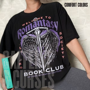 Puede incluir: Una camiseta negra de manga corta con un gráfico de una espada y alas, con el texto "WELCOME TO ROMANTASY SOCIETY BOOK CLUB BECAUSE, WINGSPAN MATTERS" y "COMFORT COLORS" impreso en la esquina superior derecha.