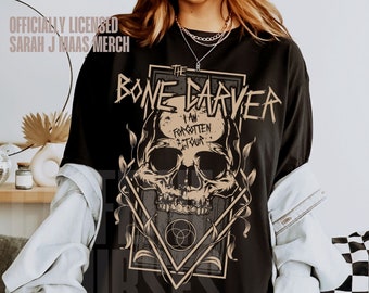 May include: Black t-shirt featuring a graphic print of a skull with the text "The Bone Carver I Am Forgotten Tour" in a distressed font.