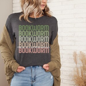 May include: A dark gray t-shirt with the word "BOOKWORM" repeated five times in a retro style font. The text is in shades of green, yellow, and pink.