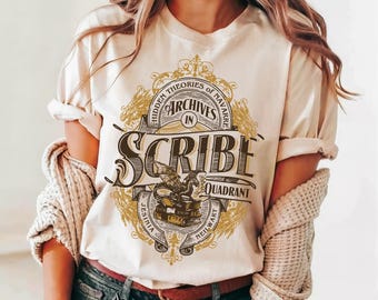 May include: A cream-coloured t-shirt featuring a graphic print with the text "Hidden Theories of Navarre", "Archives in Scribe Quadrant", "Jesinia", and "Neilwart". The design includes a dragon perched on a stack of books within an ornate frame.