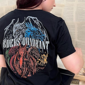 May include: Black t-shirt featuring a graphic of four dragons in different colours and the text "Riders Quadrant".