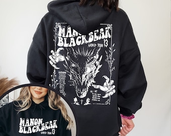 May include: Black hooded sweatshirt with a white graphic print of a dragon with the text "Manon Blackbear World Tour 13" on the back. The front of the sweatshirt has the same text in a smaller size.