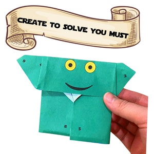 Może przedstawiać: Zielona żaba origami z uśmiechającą się twarzą i ż&oacute;łtymi oczami. Żaba jest ponumerowana 2, 5, 8 i 9 na swoim ciele. Tekst "CREATE TO SOLVE YOU MUST" jest napisany na zwoju nad żabą.