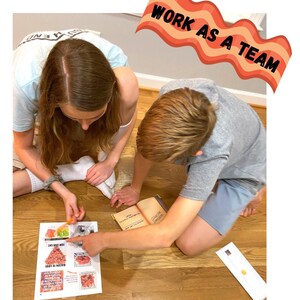 Op de afbeelding: Twee kinderen werken samen aan een puzzel. De puzzel is een afbeelding van een bacon cheeseburger. De kinderen zitten op de vloer en kijken naar de puzzelstukjes. De tekst "Werk als een team" staat op een banner in de rechterbovenhoek van de afbeelding.