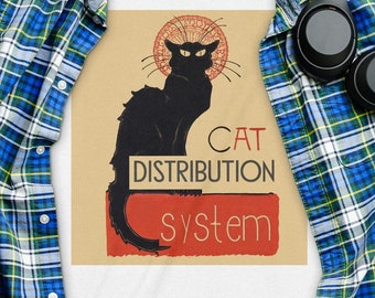 May include: White t-shirt with a black cat graphic and the text "CAT DISTRIBUTION system". The cat is in a stylized art deco design with a halo around its head. The shirt is laid out on a plaid flannel shirt and a wooden surface.