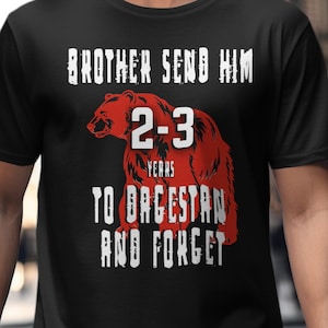 Op de afbeelding: Zwart t-shirt met een rode beer afbeelding en witte tekst: "BROTHER SEND HIM 2-3 YEARS TO DAGESTAN AND FORGET". Het ontwerp gebruikt een verweerde lettertype en een berenillustratie.