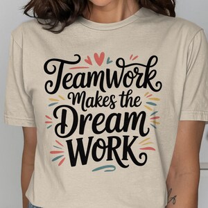 Può includere: T-shirt beige con la scritta "Teamwork Makes the Dream Work" in corsivo nero. Il design include accenti colorati in rosso, giallo e blu. È un capo di abbigliamento casual.