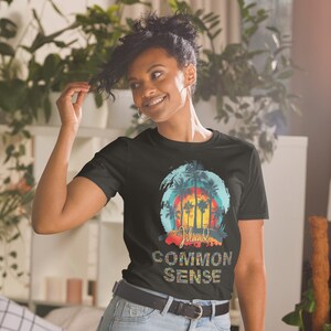May include: Black t-shirt featuring a graphic of palm trees and a sunset on a blue and white background. The text "Island Common Sense" is printed below the graphic.