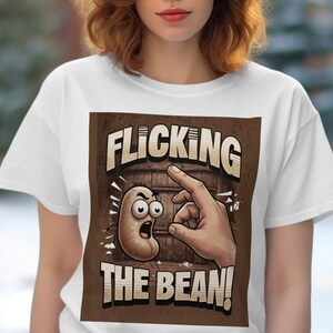 Puede incluir: Camiseta blanca con un gráfico marrón de una mano haciendo clic en un frijol de dibujos animados con el texto "FLICKING THE BEAN!"