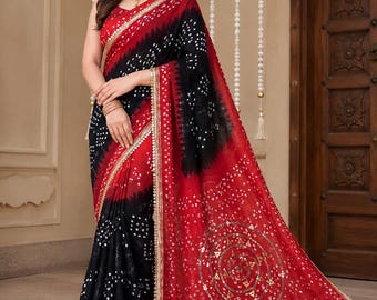 May include: A red and black saree featuring a traditional bandhani tie-dye pattern with white dots. The garment includes a gold-toned border and a large circular motif on the pallu embellished with metallic sequins and small mirrors.