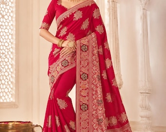 May include: A vibrant red saree featuring intricate gold and dark floral embroidery throughout the fabric. The garment includes a wide, ornate border with a geometric pattern and rose motifs, paired with a matching blouse with elbow-length sleeves.