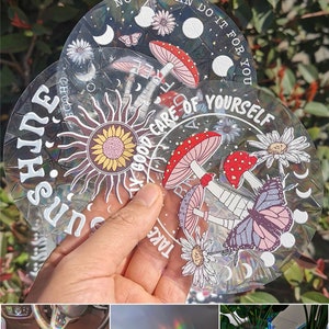 May include: Three iridescent holographic stickers with a whimsical design featuring mushrooms, butterflies, flowers, and the sun. The stickers have the text "Take good care of yourself" and "Sunshine" on them.