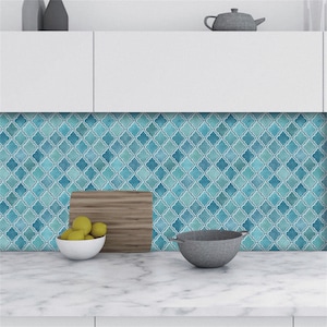 Op de afbeelding: Een keukenachterwand met een geometrisch patroon in blauw en wit. Het patroon bestaat uit kleine, herhalende vierkanten met een klaverbladontwerp in het midden. De achterwand is geïnstalleerd boven een wit aanrecht.