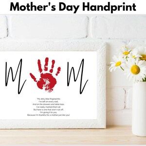 Peut inclure: Un cadre blanc avec une empreinte de main rouge au centre du mot "MOM" en noir. Le cadre est sur un mur en briques blanches avec un vase de fleurs blanches sur une surface en bois. Le texte sous l'empreinte de main dit : "Mes petits doigts sales J'ai laissé sur chaque mur Et sur les tiroirs et les dessus de table Je les ai vraiment marqués tous Mais voici un qui ne s'effacera pas Je te le donne Parce que je suis reconnaissant pour une mère comme toi !"