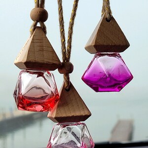 Puede incluir: Tres ambientadores de coche de madera con cuerdas colgantes. Cada ambientador tiene una botella de vidrio transparente con un l&iacute;quido rosa, rojo o morado en su interior. Las botellas tienen forma de diamante.