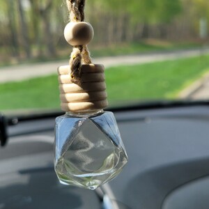 Puede incluir: Un adorno de vidrio transparente en forma de estrella con una parte superior de madera y una cuerda para colgar. El adorno est&aacute; colgado del espejo retrovisor de un coche.