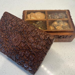 May include: A wooden box with intricate floral carvings. The box is open and reveals four compartments filled with various items, including dried fruit and nuts.