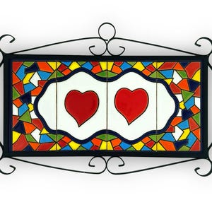 May include: A rectangular wall plaque with two red hearts on a white background, framed by a black wrought iron design. The border is a mosaic of colourful geometric shapes in red, blue, yellow, and green.
