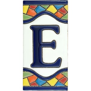 Può includere: Piastrella in ceramica rettangolare con una grande lettera "E" blu navy su sfondo bianco. La piastrella è bordata con un bordo blu navy e motivi a mosaico decorativi in vari colori, tra cui giallo, arancione e verde.
