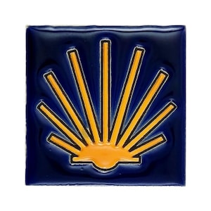 May include: Square ceramic tile with a glossy finish. The tile features a stylized yellow sunburst design against a deep blue background. The sunburst design has black outlines. The tile is a decorative item.