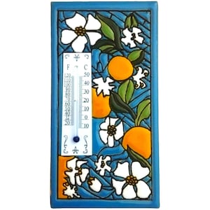 May include: A rectangular ceramic thermometer with a blue border, featuring a design of oranges, white flowers, and green leaves against a blue background. The thermometer displays Fahrenheit and Celsius scales.