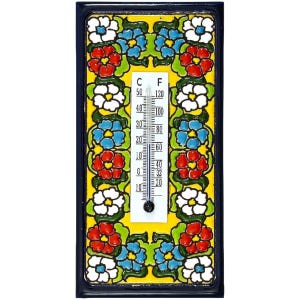 Op de afbeelding: Een rechthoekige keramische thermometer met een gele achtergrond en een bloemenrand. De rand heeft rode, witte en blauwe bloemen met groene bladeren. De thermometer geeft zowel Celsius- als Fahrenheit-schalen weer.