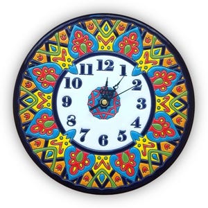 May include: A round, ceramic wall clock with a vibrant, hand-painted design. The clock face is white with black numerals and hands. The border features a repeating pattern in red, blue, yellow, and green. The clock measures approximately 12 inches in diameter.