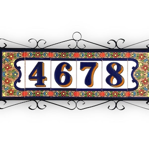 Puede incluir: Placa decorativa con el número 4678. Los números azules con borde naranja sobre fondo blanco. El marco es de hierro forjado negro con azulejos florales coloridos. Medidas en centímetros.