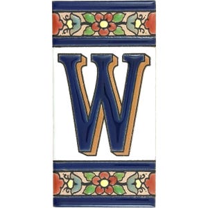Puede incluir: Una baldosa cerámica rectangular con la letra "W" en azul marino con contorno beige, sobre fondo blanco. La baldosa está bordeada por una banda azul marino con un diseño floral en rojo, verde y amarillo.