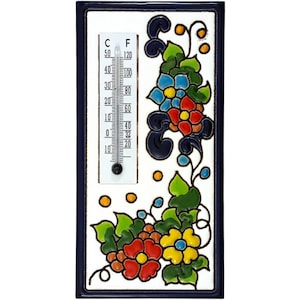 Pode incluir: Um termómetro de cerâmica retangular com uma face branca e uma borda azul escura. O termómetro exibe as escalas Celsius e Fahrenheit. Desenhos florais coloridos em vermelho, azul e amarelo adornam os cantos, adicionando um toque decorativo.