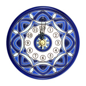 Op de afbeelding: Ronde keramische wandklok met een blauw en wit bloemmotief. De wijzerplaat heeft zwarte wijzers, een gouden midden en witte cijfers. De buitenrand van de klok is diepblauw.