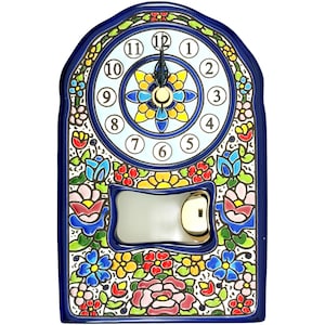 Può includere: Un orologio da parete in ceramica con bordo blu e quadrante bianco. Il quadrante ha numeri neri e lancette nere. L'orologio è decorato con motivi floreali colorati in rosso, blu, giallo e rosa.