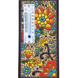 May include: A rectangular ceramic thermometer with a floral design. The thermometer displays both Fahrenheit and Celsius scales. The background is beige with colorful flowers in red, yellow, blue, and green. The frame is dark blue.