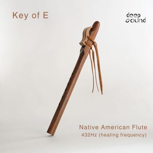Puede incluir: Una flauta nativa americana de madera marrón con una correa de cuero y una incrustación turquesa. La flauta está en la tecla de E y toca a 432 Hz, que se considera una frecuencia de curación. El texto "deep sound" está en la esquina superior derecha de la imagen.