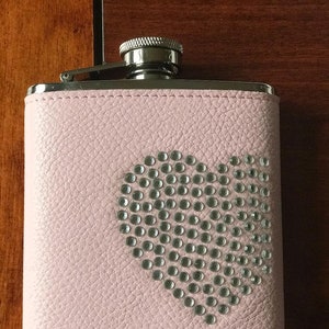 May include: A pink leather hip flask with a silver lid and a heart-shaped design made of rhinestones.