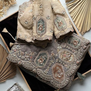 May include: A beige long-sleeved blouse with intricate embroidery and scalloped cuffs paired with a matching grey shawl featuring ornate floral patterns, sequin embellishments, and decorative rectangular panels with metallic thread detailing.