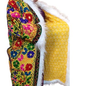 Peut inclure: Un manteau jaune avec des broderies florales colorées, avec des fleurs rouges, bleues et roses. Le manteau a une bordure en fausse fourrure blanche et une doublure jaune à motifs. Les manches sont visibles, mettant en valeur la broderie et le design.
