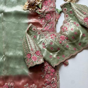 May include: A green and pink embroidered saree and blouse set. The blouse is a light green with pink floral embroidery and scalloped edges. The saree features a gradient of green to pink with intricate floral embroidery along the border.