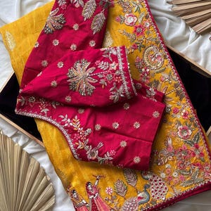 May include: A yellow and red embroidered saree with detailed floral and peacock designs. The red blouse pieces have elaborate floral patterns. The saree is likely made of silk or a similar luxurious fabric. The embroidery is very detailed and intricate.