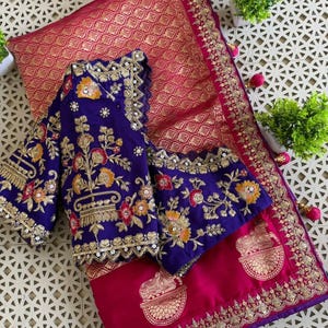 May include: A vibrant magenta and gold sari with a matching royal blue blouse. The sari features intricate gold embroidery and a repeating pattern. The blouse is adorned with floral and gold thread embroidery.