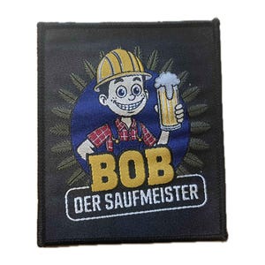 Könnte beinhalten: Gestickter Aufnäher mit einem Cartoon-Bauarbeiter, der einen Bierkrug hält. Die Figur trägt einen gelben Helm, ein rot kariertes Hemd und eine blaue Latzhose. Der Aufnäher trägt den Namen "BOB" und den Schriftzug "DER SAUFMEISTER" in Gold und Weiß auf schwarzem Hintergrund.