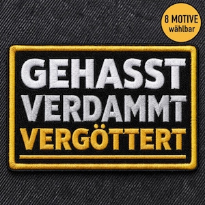 Könnte beinhalten: Ein rechteckiger, bestickter Aufnäher mit schwarzem Hintergrund und goldenem Rand. Der Text GEHASST VERDAMMT ist in Weiß gestickt, während das Wort VERGÖTTERT darunter in Gold gestickt ist, gefolgt von einer goldenen Linie.