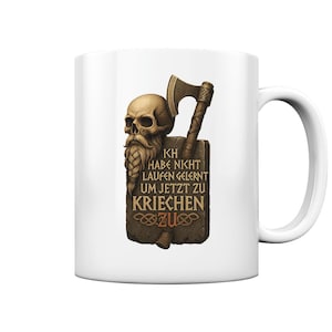 Può includere: Tazza in ceramica bianca con un'illustrazione dettagliata di un teschio con barba intrecciata, un'ascia e il testo tedesco "ICH HABE NICHT LAUFEN GELERNT UM JETZT ZU KRIECHEN ZU". La tazza ha un manico curvo.