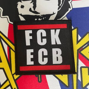 Könnte beinhalten: Schwarzer quadratischer Aufnäher mit dem weißen Text "FCK ECB" und einem roten Streifen oben und unten. Der Aufnäher ist vor einem Hintergrund mit Union Jack-Design und Grafik platziert.