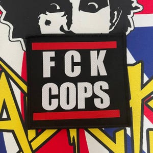 Puede incluir: Parche negro con texto blanco que dice "FCK COPS" con una franja roja arriba y abajo del texto.