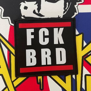 Könnte beinhalten: Schwarzer Patch mit rotem Rand und weißem Text, der "FCK BRD" lautet.